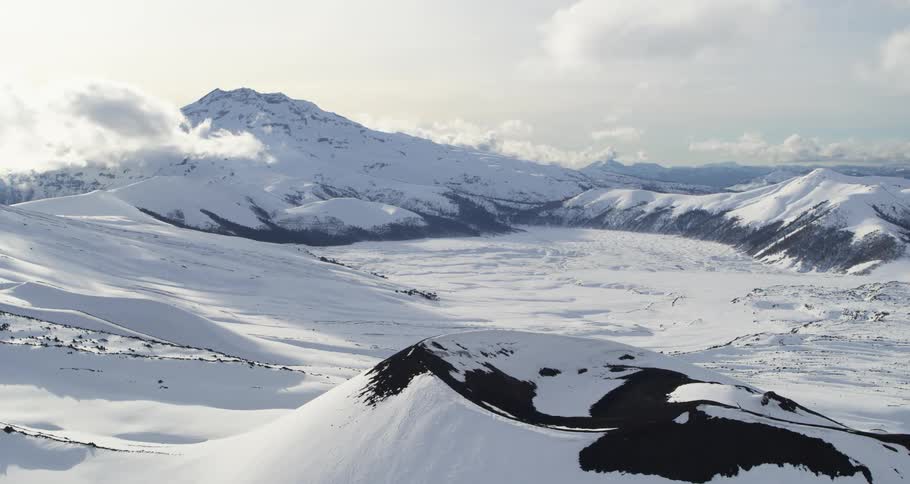Aerial of a volcano in front of a snowy mountain range