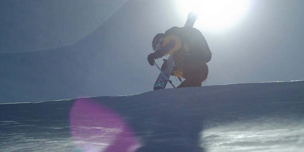 A skier holds his skis while walking against blowing wind and snow