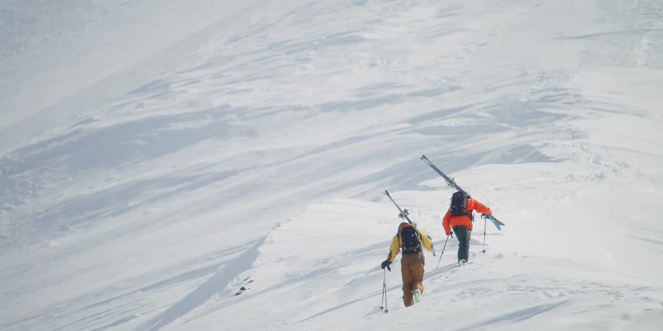 Two skiers climb up a mountain