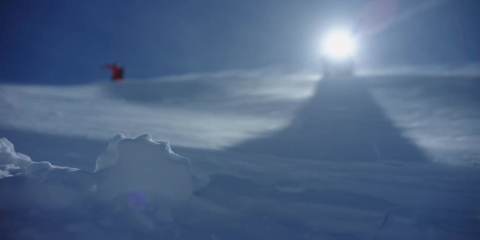 A pair of hikers walking against drifting snow across a snowy slope