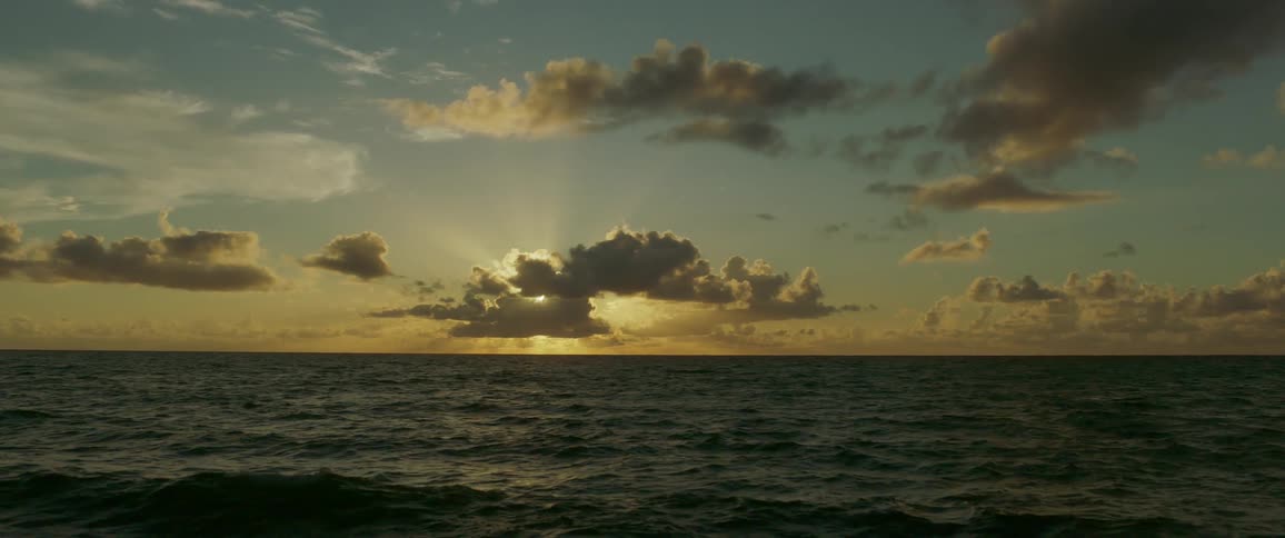 Sun casting sunbeams from behind clouds over horizon on ocean