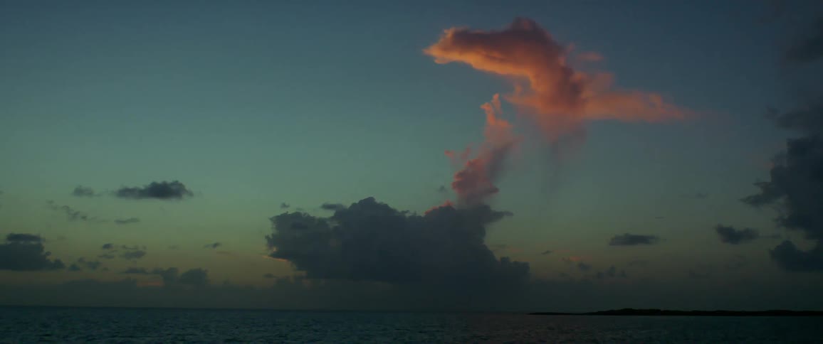 The sun sets over the ocean with a red cloud surrounded by blue sky