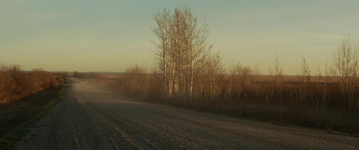 A pickup truck kicks up dust as it drives down a narrow gravel road