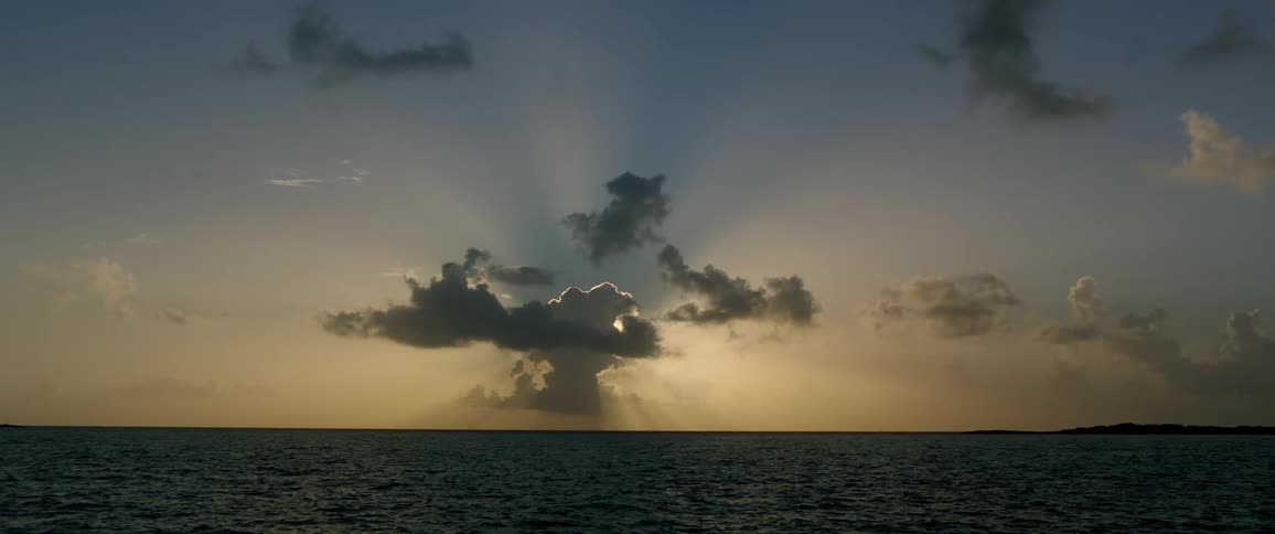 Sun casts sunbeams from behind large cloud over ocean