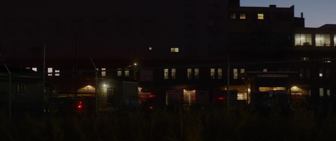 Semi truck drives through lot behind building with lit windows at night
