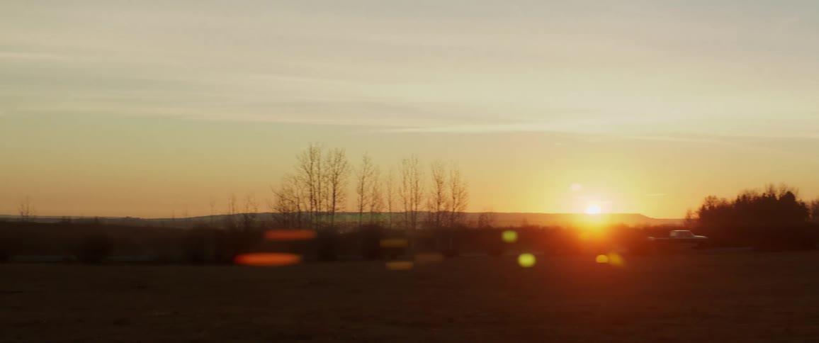 Pickup truck drives down country road in front of sunset
