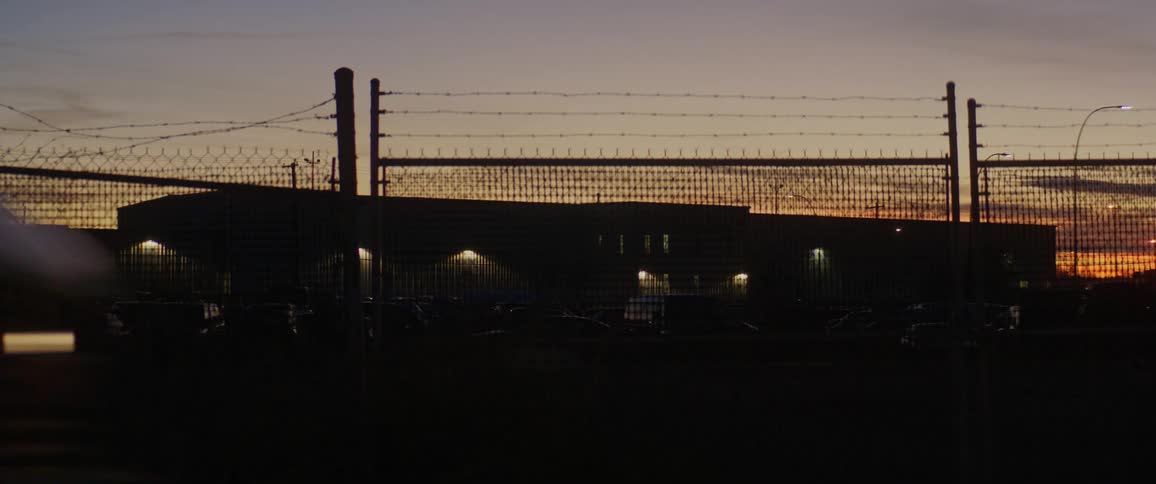 Vehicle drives past a fence at dusk