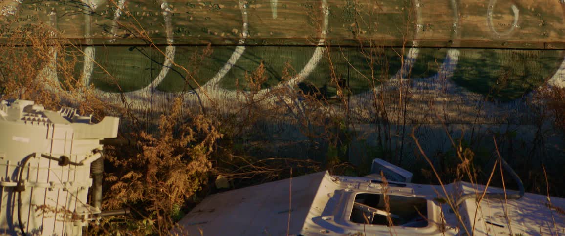 Large electronic machinery stand in overgrown lot near green and white painted wall