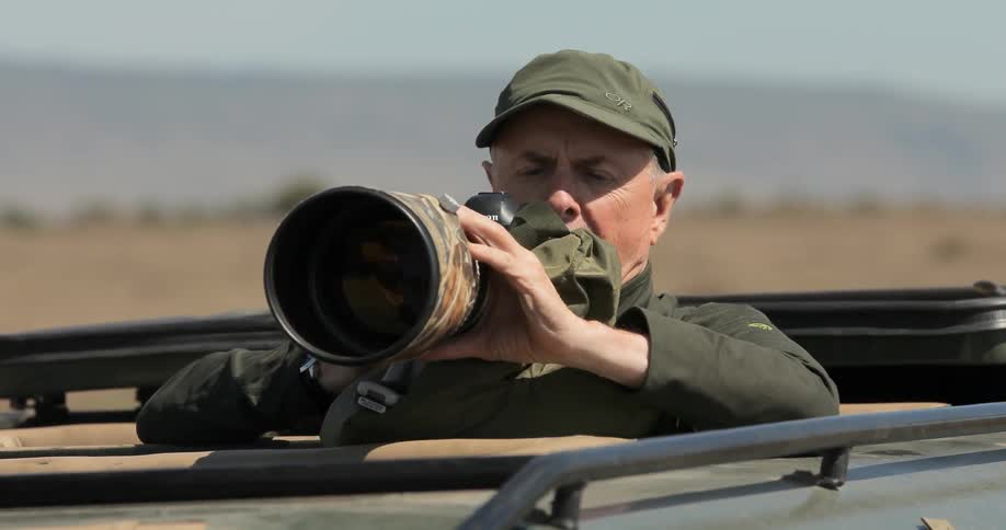 A man is photographing from the top of a vehicle