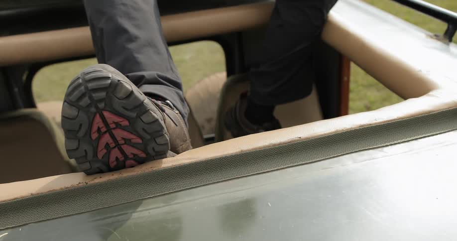 View of someone's feet and legs as they dangle through the sunroof of a vehicle travelling through a grassy area