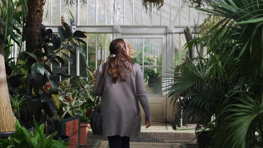A white woman walks through a greenhouse and looks at the plants