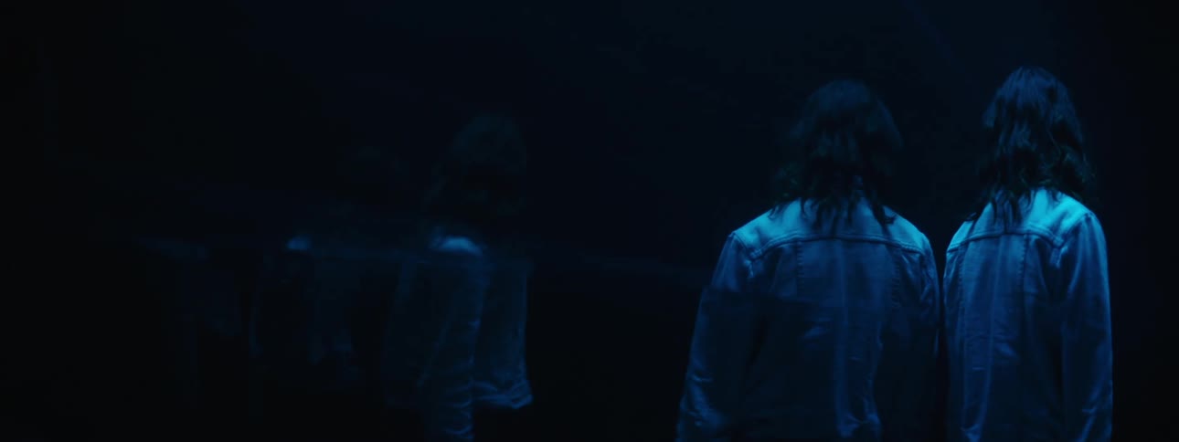 A white woman in a denim jacket walks by a mirror