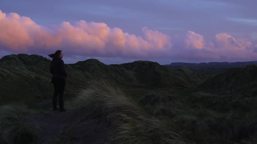 A woman stands and looks out across the land