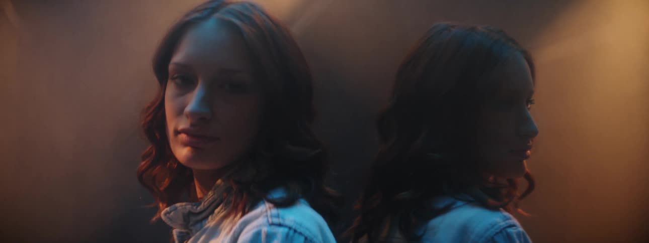 Woman leans against a mirror and stares at the camera in a foggy room