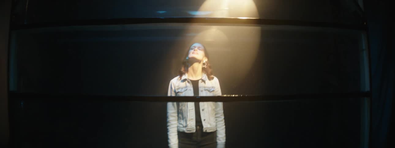 A woman stands with her head tilted back and a spot light shining down on her