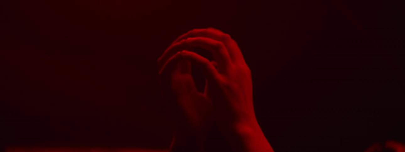 A woman taps and runs her hand down a mirrored wall lit with a red light