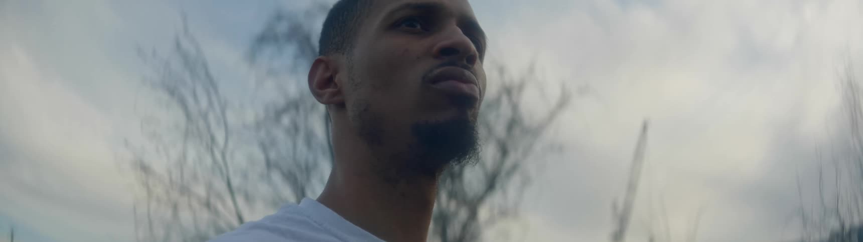 A black man with a beard stands outside and looks around
