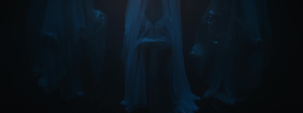 Three figures draped in sheer fabric in a dark room