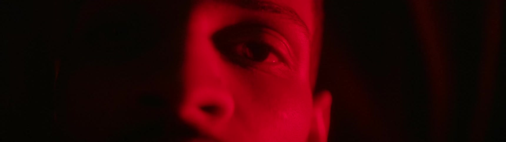 A persons face is mostly in shadow with red light glowing