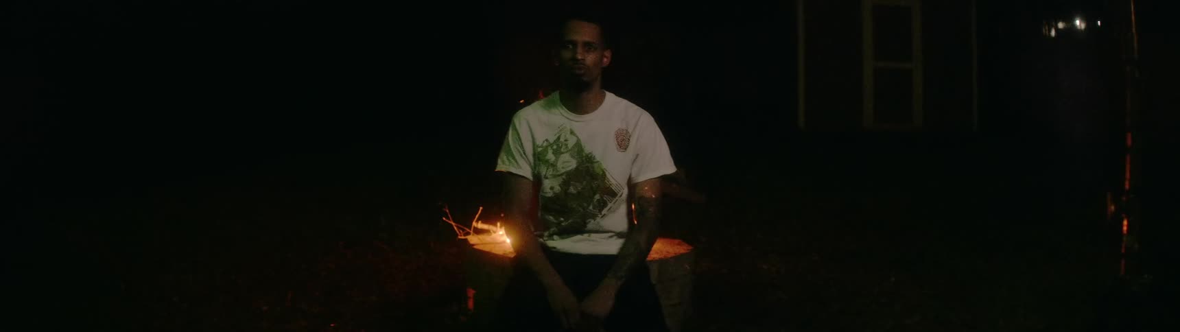 A man sits as fire burns in a fire pit behind him