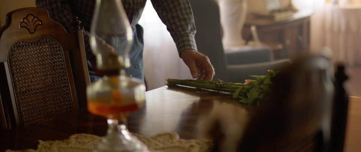 An old white man walks to a table and picks up a bouquet