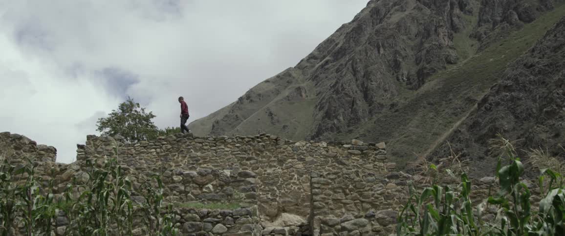 Teenager walks across ruins of rock wall beneath mountain
