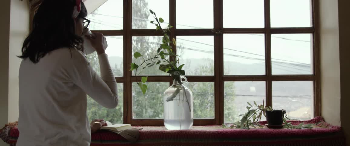 A young woman looks out the window and picks up her coffee cup and takes a drink