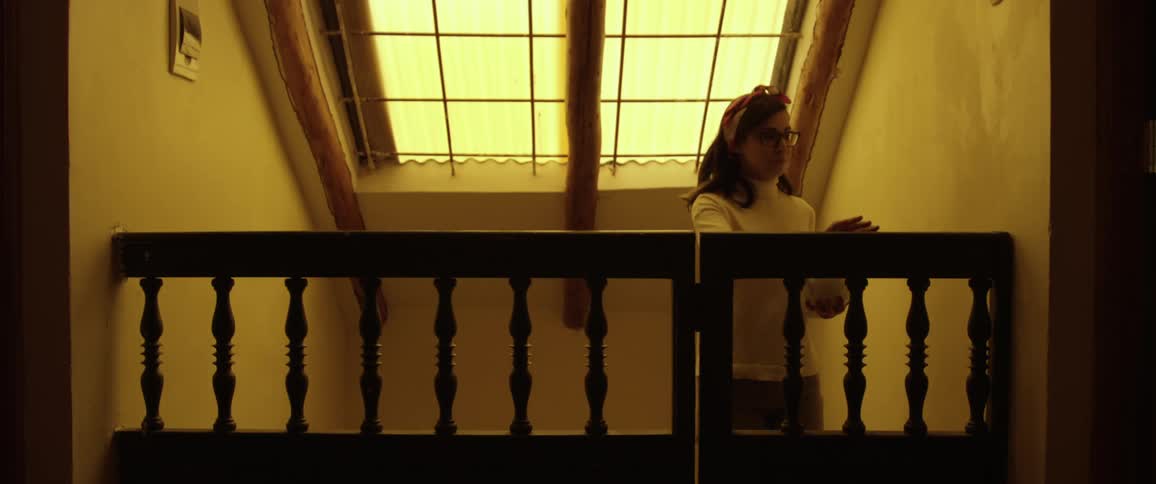 A woman walks up the steps of her house and through a gate holding a tea kettle
