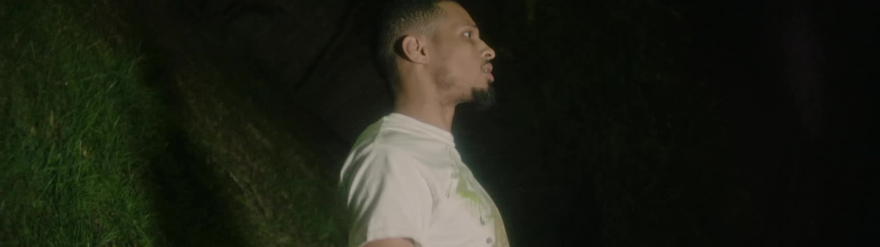 A man stands against a moss covered wall as a light repeatedly flashes around him