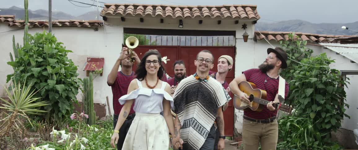 A group of people walk with instruments outside a small building