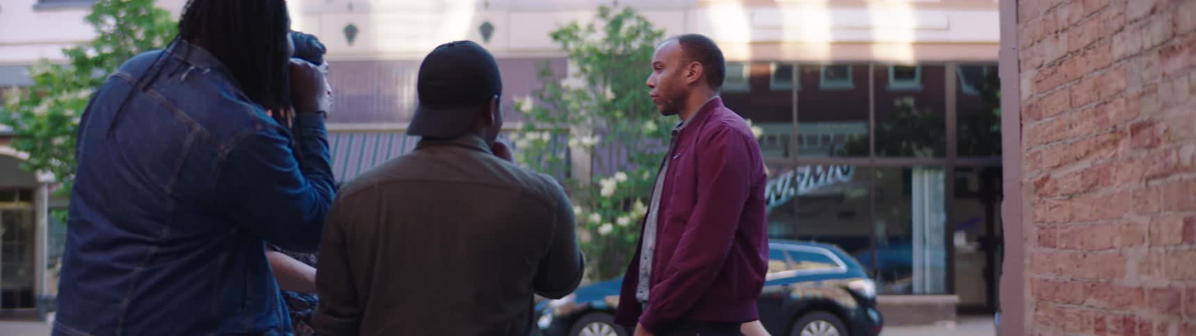 A group of friends talk on the street corner and then one follows a girl as she walks by