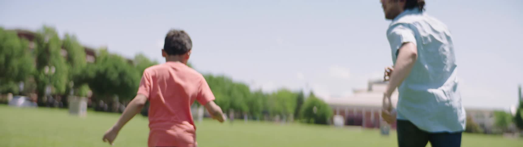 An adult and a child run over a grassy field playing soccer