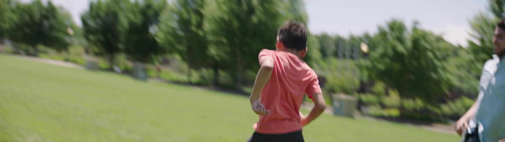 Father and son play soccer in park on sunny day