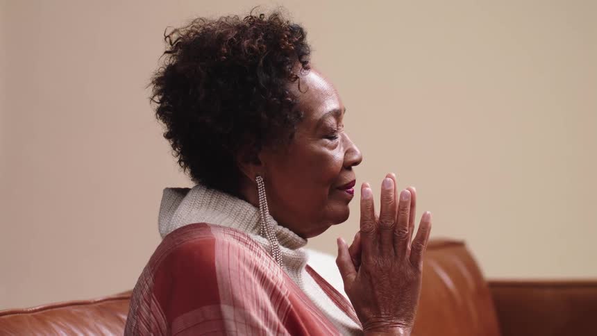 Elderly woman sitting on leather couch and praying
