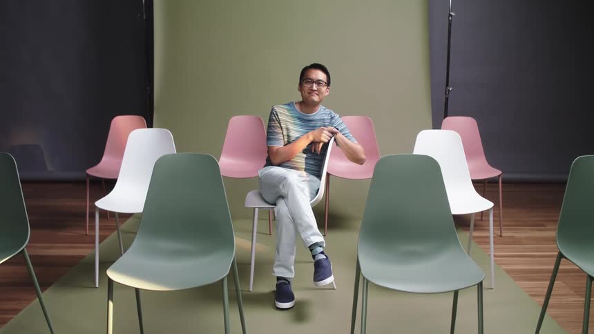 An asian man sits in a chair and smiles for a picture