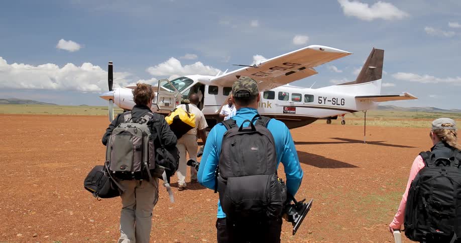 A group of passengers carrying backpacks and gear walk toward a small plane