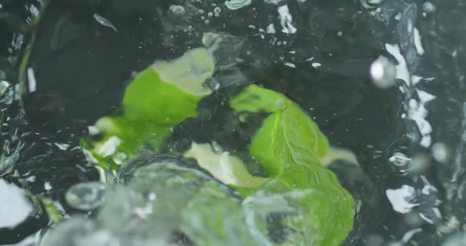 Hands drop lime wedges and leaves into a sink of clear water