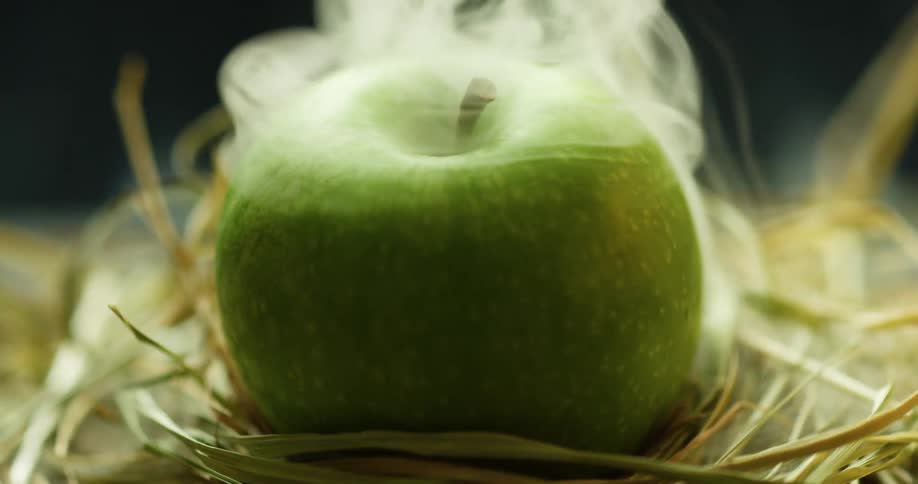 An apple with mist over it sits in straw as it rotates in a studio