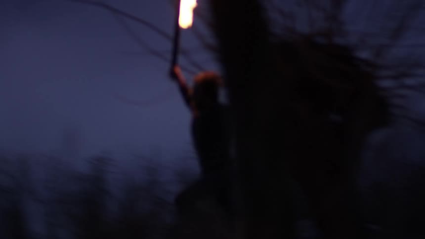 Man holding a blazing torch runs in the forest at dusk