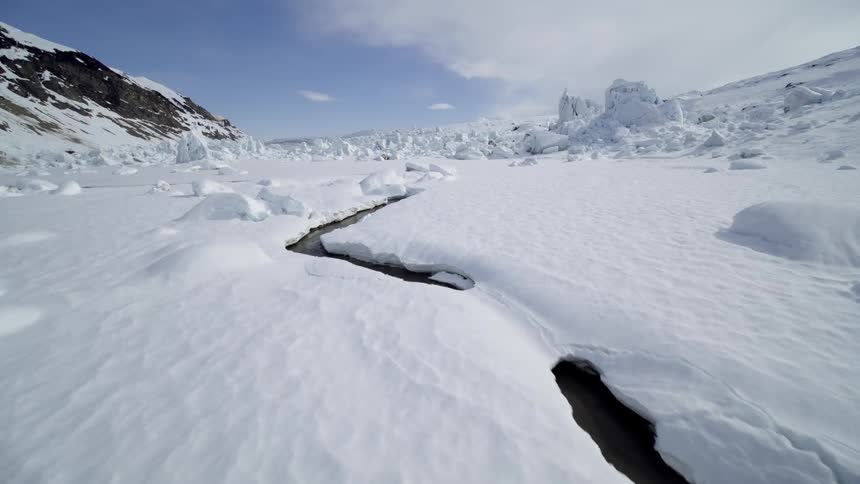 A valley littered in blocks of ice and frozen streams between mountains in the arctic