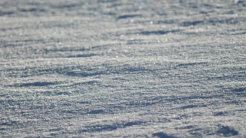 Snow drifts across ground blown by wind