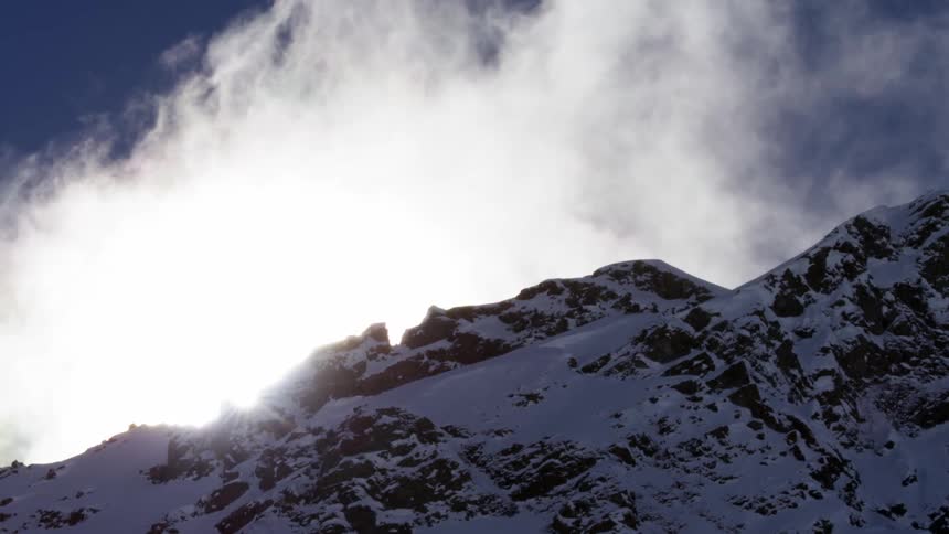 Sun shining behind tall snow covered rugged mountain range