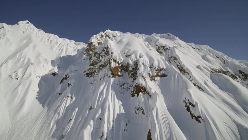 A stony mountain slope covered in snow under a clear blue sky