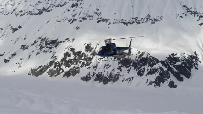 A helicopter flies through the mountains