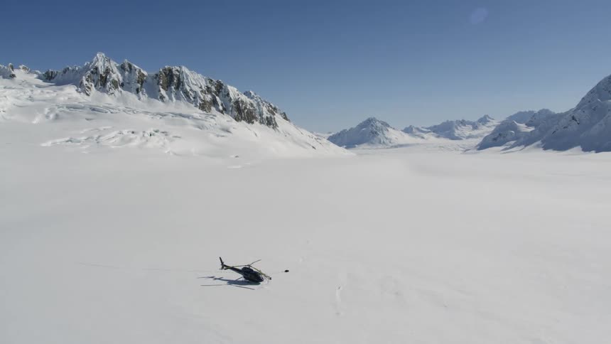A helicopter sitting on a snow covered flat area between rocky jagged peaks