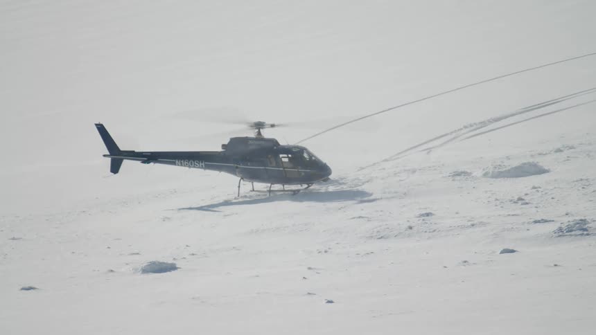 A helicopter on snow covered land with a person outside it