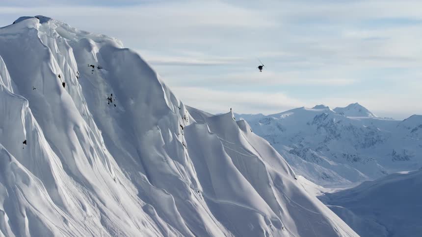 A helicopter flies near a mountain peak and then turns and banks downward