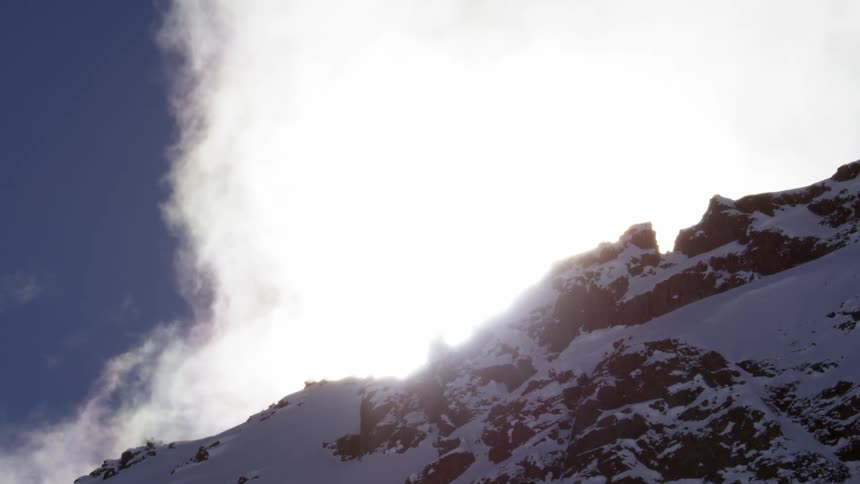 White clouds move over a snowy mountain ridge
