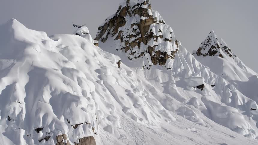 Helicopter near tall rocky mountain peak and snow covered slope