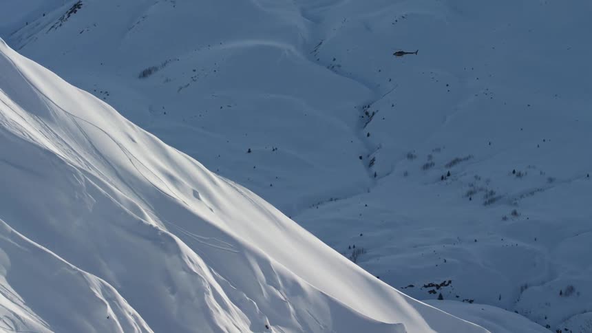 A helicopter flies over a snow covered mountain valley